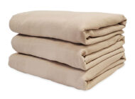 Stack of Dempsey Uniform medical linen bedspreads in beige color