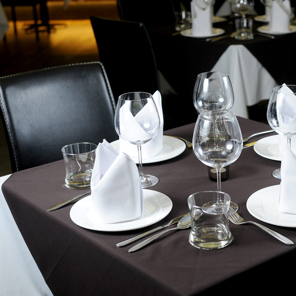 White Dempsey Uniform cloth napkins folded decoratively in place settings with glassware and a black tablecloth
